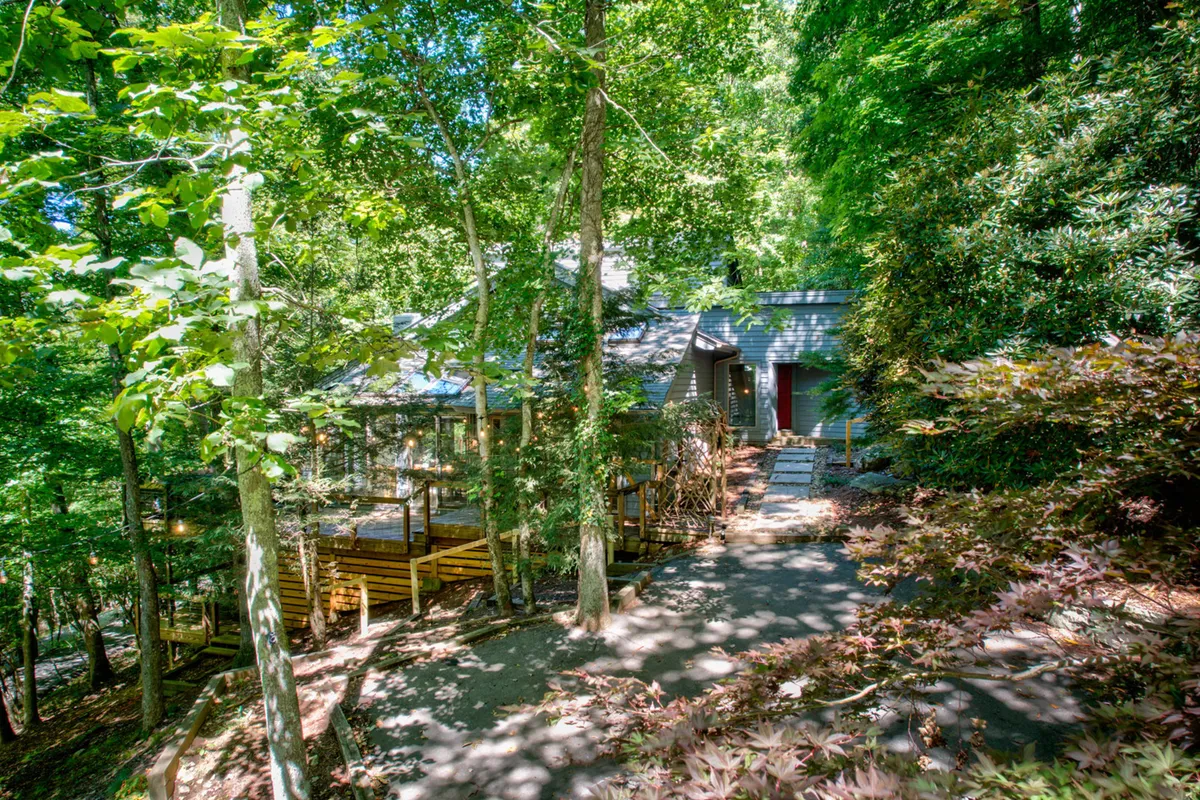 A view of the wooden deck and the front entrance of Deerwood Manor, framed by mature trees. The setting offers a tranquil forest backdrop and hints at the spacious outdoor areas ideal for group gatherings or nature walks.