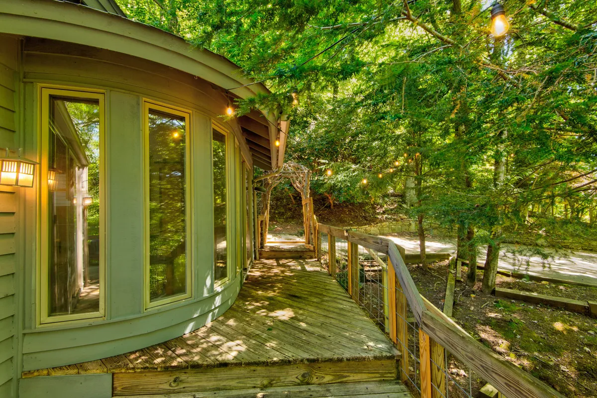 A tranquil exterior shot featuring a curved wooden walkway leading to a building with large windows, nestled among lush greenery. The space is illuminated with soft outdoor lighting, and the natural surroundings evoke a peaceful, inviting atmosphere ideal for outdoor exploration and relaxation.