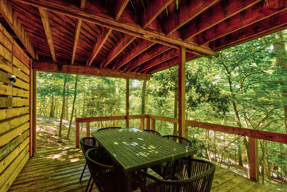 A serene exterior deck scene featuring a wooden dining table surrounded by woven chairs and lush greenery. This inviting outdoor space is perfect for al fresco dining, evening snacks, or simply cheering on the game room action from just outside the sliding doors.