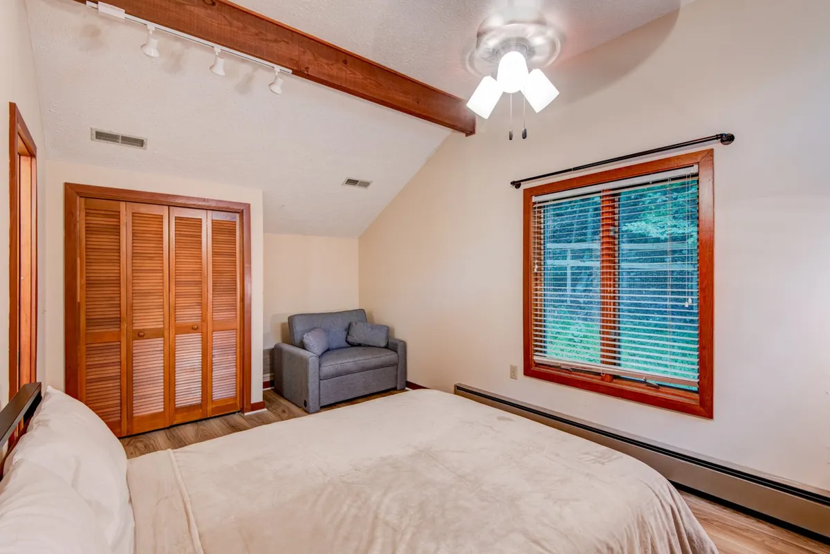 A cozy bedroom with a bed, sofa, window letting in natural light, and a closet. The room feels inviting and tranquil, ideal for relaxation or reading after a day of adventure.