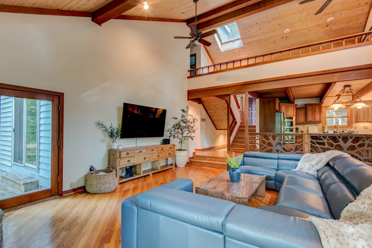 This inviting living area features a large sectional sofa, a wooden coffee table, a television on a console, a skylight, and a staircase leading to the upper level. The space radiates comfort and is ideal for relaxing, entertaining guests, or gathering for games and conversation.