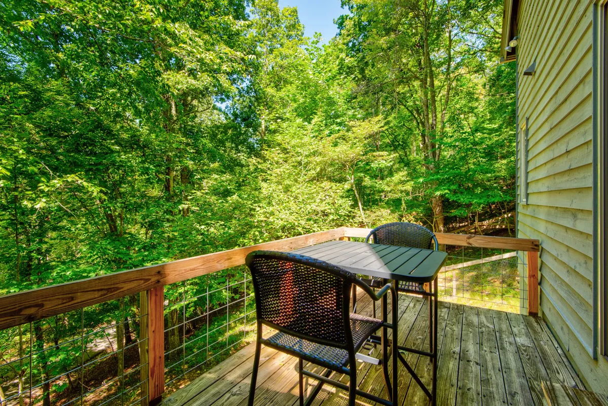 This image focuses on a wooden deck with black chairs and lush green foliage, offering a tranquil spot for morning coffee, reading, or intimate gatherings. The view highlights the deck's seamless connection to the natural surroundings, enhancing a sense of serenity and outdoor enjoyment.