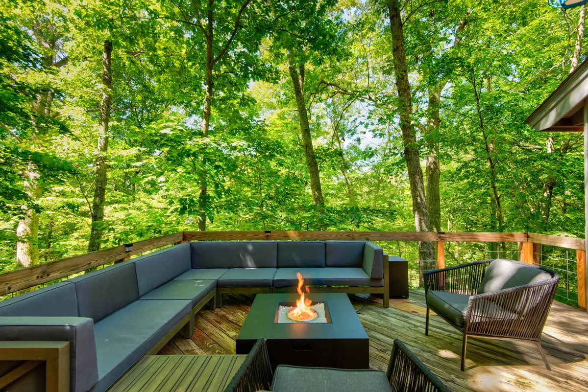 An inviting outdoor fire pit area surrounded by comfortable sofa seating, nestled within lush greenery. The space is perfect for evening gatherings, stargazing, and connecting with friends or family members of all ages.