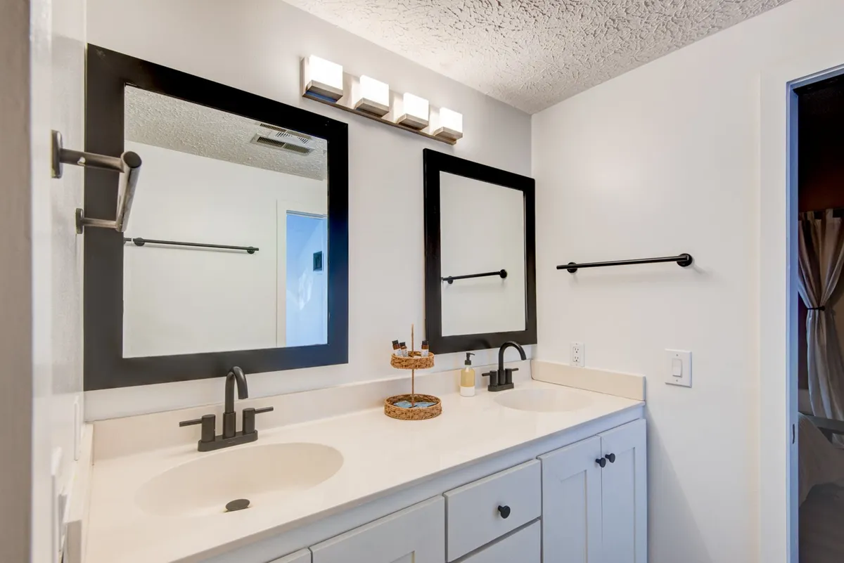A bright bathroom with double sinks, large mirrors, a decorative tray, and welcoming lighting. The space feels both functional and fresh, supporting self-care routines and shared morning rituals.