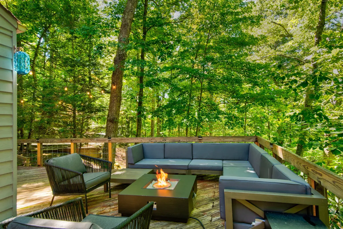 An inviting outdoor fire pit area surrounded by sectional seating, nestled among mature trees. The scene is designed for relaxation and socializing, offering a cozy spot to unwind after a day of outdoor fun with your dog.